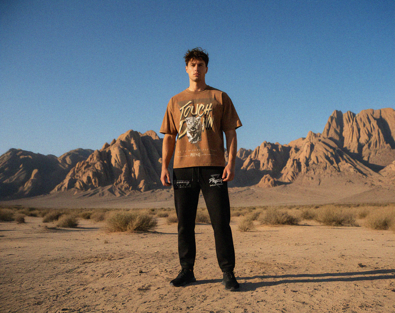 Person wearing a brown t-shirt with graphic design in a desert landscape